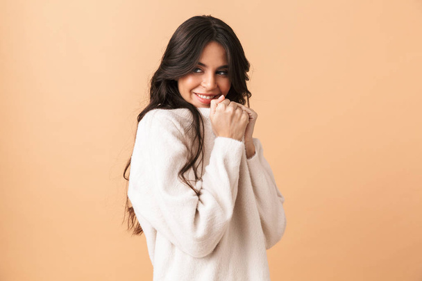 Portrait of a lovely brunette woman wearing sweater standing isolated over beige background - Foto, Imagem