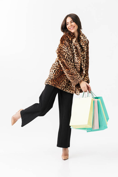 Full length of a beautiful woman wearing leopard fur coat standing isolated over white, carrying shopping bags - Fotó, kép