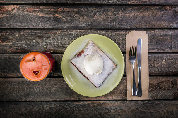 A kerámia tányér az evőeszközök és a pohár ital szolgált rétes vanília fagylalttal és meggy. - Fotó, kép