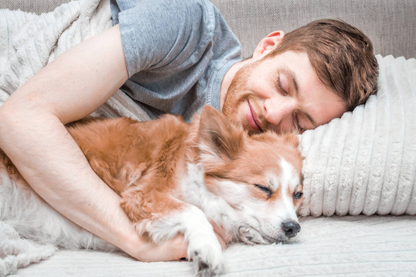 fiatal férfi és egy kutya alszik egy ágyban. Vértes portré. Koncepció a hétvégén - Fotó, kép