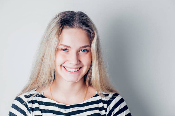Beautiful smiling woman with clean skin, natural makeup and white teeth on white background with copy space. Attractive young blonde girl with blue eyes looking at camera - Zdjęcie, obraz