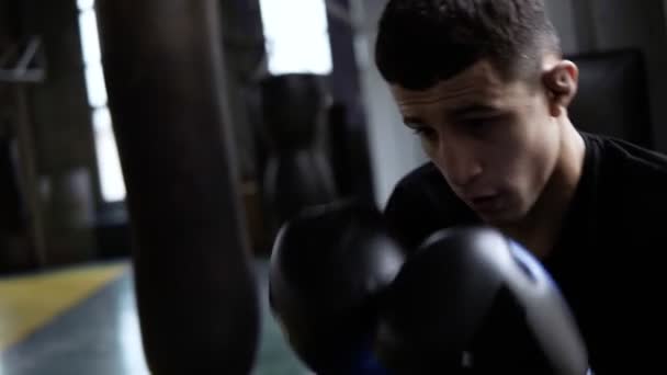 Handhelded footage of young boxers training. Dark haired man hitting the boxing bag, hard kicks. Motivation in sport. Old style gym, daytime. Close up - Materiał filmowy, wideo