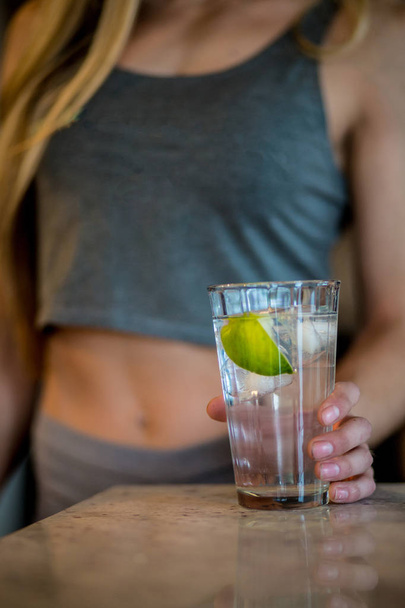 Fit woman holding a glass of icewater with lime. - Photo, Image