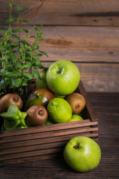 Healthy food background. Concept of healthy food. Fresh green fruits in box on dark wooden background. Set of green fruits for healthy diet and detox: apple, lime, kiwi, mango, carambola and mint. - Foto, Imagen