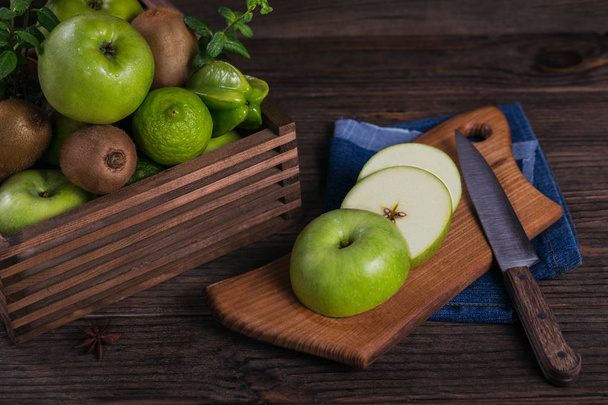 Az egészséges ételek fogalmát. Friss zöld gyümölcsök egy doboz, zöld alma, vágódeszka. Sötét fából készült háttér. Készlet-ból egészséges diéta és méregtelenítő zöld gyümölcsök: alma, lime, kiwi, mangó, karambola és menta - Fotó, kép