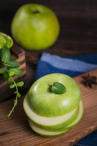 Concept of healthy food. Sliced green apple on cutting board and fresh green fruits in a box. Dark wooden background. Set of green fruits for healthy diet and detox: apple and mint. - Photo, Image