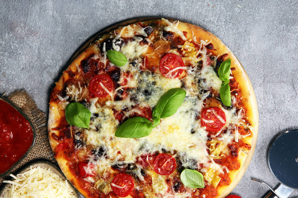 Pizza italiana vegetariana com queijo derretido, tomates vermelhos e manjericão verde sobre uma mesa decorada com queijo, tomate e tomate cereja vermelho
 - Foto, Imagem