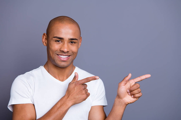 Close up photo healthy masculine dark skin he him his macho bald head eyes arms fingers point to empty space show low cool cheap prices wearing white t-shirt outfit clothes isolated grey background - Photo, Image