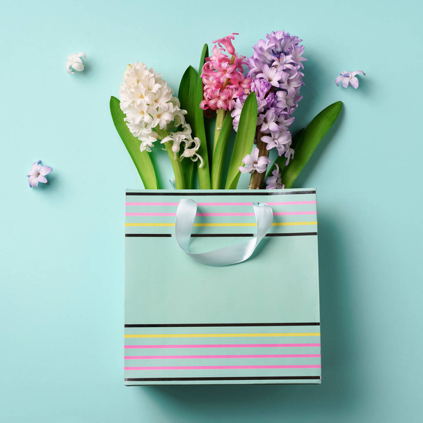 Spring hyacinth flowers in shopping paper bag on blue punchy pastel background. Square crop. Spring, summer or garden concept. Creative layout. Top view, flat lay. Square crop - Photo, Image