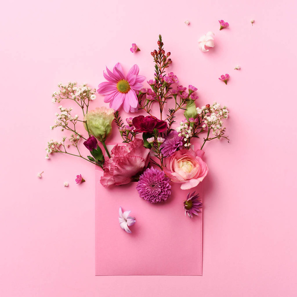 Pink envelope with spring flowers. Floral composition, creative layout. Flat lay, top view. Spring, summer or garden concept. Present for Woman day. Square crop. - Foto, Imagem