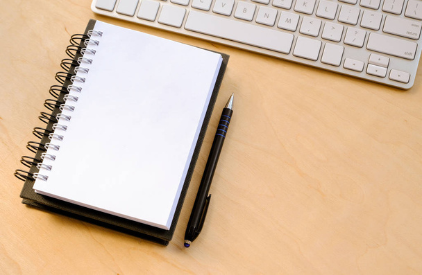 An opened notebook, a keyboard and a black pen on the desktop, wooden background - Photo, Image