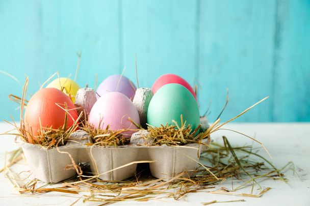 Pastel colored easter eggs in a egg box with hay as a nest against a wooden turquoise background - Photo, Image