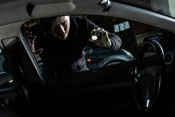 Μασκοφόροι κλέφτης σε ένα balaclava ψάχνει στο εσωτερικό του αυτοκινήτου με φακό - Φωτογραφία, εικόνα