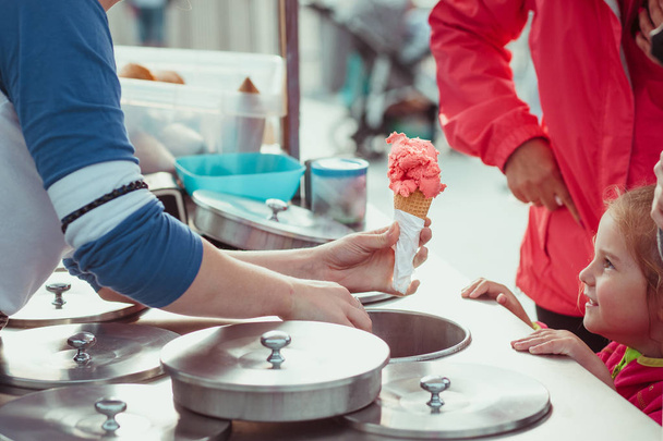 Little girl waiting for icecream. Mom buying a icecream her little daughter in a candy shop by the street. Young woman putting a scoop of pink icecream to a cone - Φωτογραφία, εικόνα
