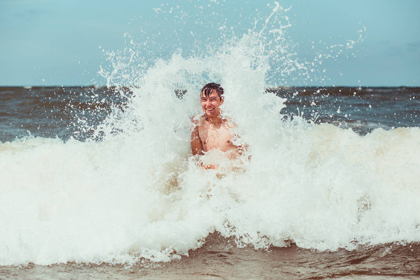 Young man enjoying the high waves in the sea during a summer vacations. Spending a summer holiday by the sea - Fotó, kép