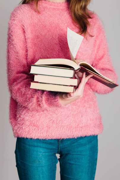 Młoda dziewczyna trzyma kilka książek. Nastolatek dziewczyna ubrana w różowy sweter i dżinsy. Pionowe zdjęcie - Zdjęcie, obraz