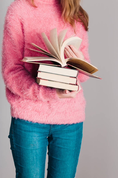 Young girl holding a few books. Teenager girl wearing pink sweater and blue jeans. Vertical photo - Fotó, kép