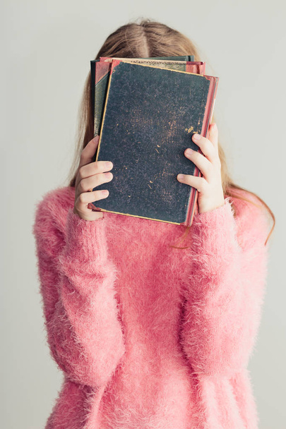 Jovencita sosteniendo libros delante de su cara. Chica adolescente vistiendo suéter rosa. Foto vertical
 - Foto, Imagen