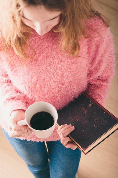 Enjoying the reading a book. Young girl holding book and cup of coffee going to relax with book. View from top - Foto, imagen