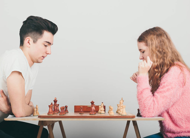 Girl and boy playing chess at home, they are concentrated on their next moves. Teenagers sitting by a table. Profile view. Copy space for text in the middle of image - Zdjęcie, obraz