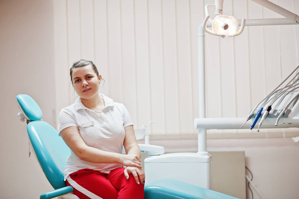 Sandalyede oturan diş hekimliği ofisinde duran kadın dişçi kadın portresi. - Fotoğraf, Görsel