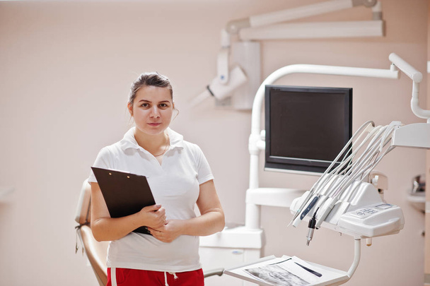Portrait of female dentist woman standing in her dentistry office with clipboard on hands. - Fotoğraf, Görsel