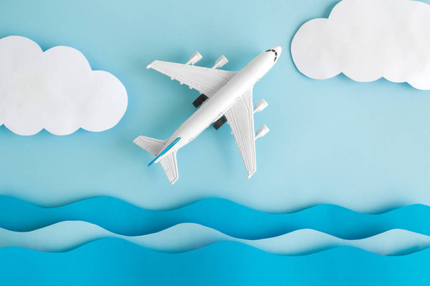Flat lay of airplane model with sea waves and clouds made of paper against pastel blue background minimal creative travel concept. - Fotografie, Obrázek