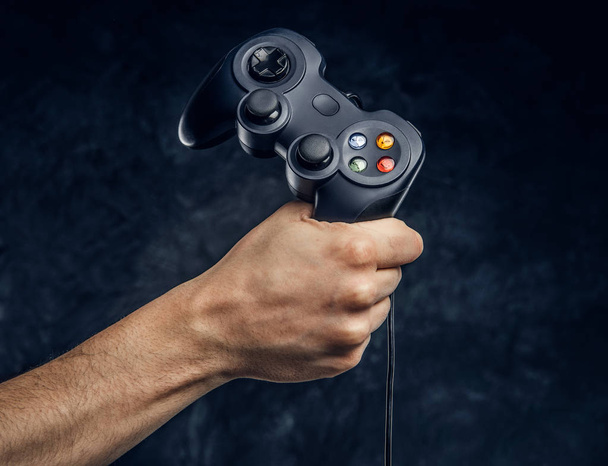 Χειριστήριο της κονσόλας παιχνιδιών βίντεο στο gamer χέρι φόντο σκούρο τοίχο - Φωτογραφία, εικόνα