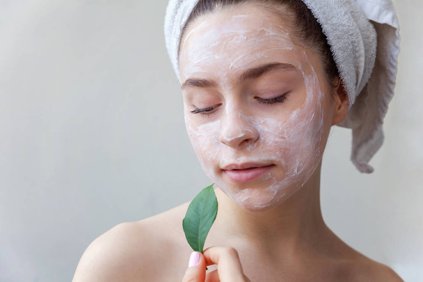 Ομορφιά πορτρέτο γυναίκας σε πετσέτα στο κεφάλι με λευκό θρεπτική μάσκα ή κρέμα στο πρόσωπο και το πράσινο φύλλο στο χέρι σε άσπρο φόντο που απομονώνονται. Περιποίηση καθαρισμού eco βιολογικά καλλυντικά spa Χαλαρώστε έννοια - Φωτογραφία, εικόνα