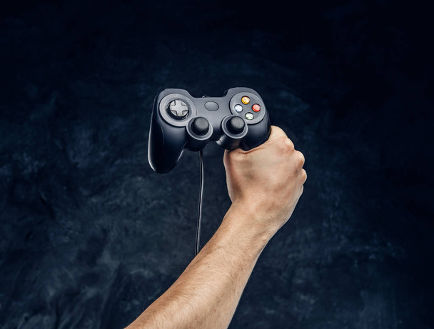 Controlador de videoconsola en mano de jugador contra el fondo de la pared oscura
 - Foto, imagen