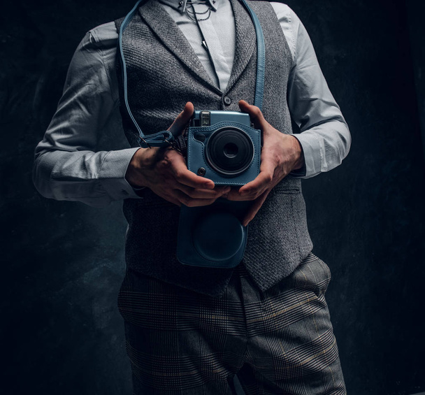 Elegantly dressed young man posing with a camera in a studio - Foto, afbeelding