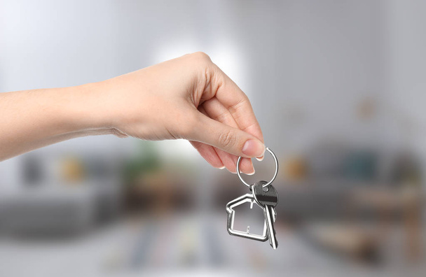 Woman holding house key on blurred background, closeup - Foto, Bild