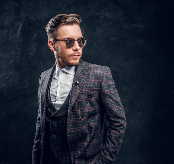 Elegantly dressed young man in sunglasses against a dark textured wall - Photo, Image