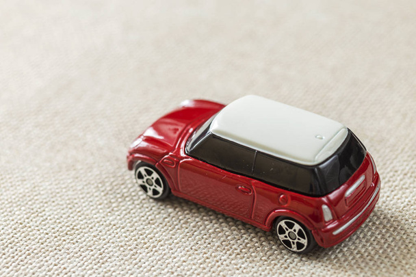 Pequeño coche de juguete infantil simple de metal rojo brillante con ventanas oscuras en lienzo beige claro, fondo de espacio de copia
. - Foto, Imagen