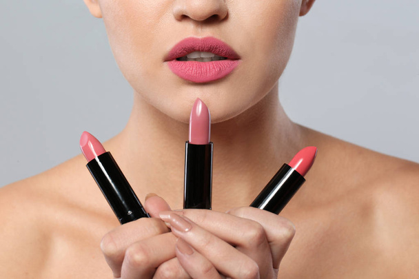 Young woman with lipsticks on gray background, closeup - Photo, image