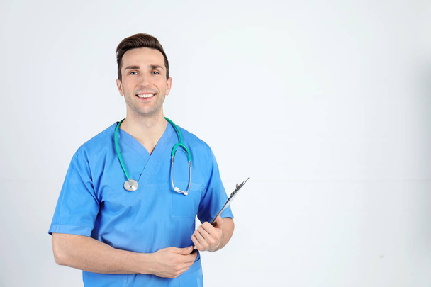 Portrait of medical assistant with stethoscope and clipboard on light background. Space for text - Фото, изображение
