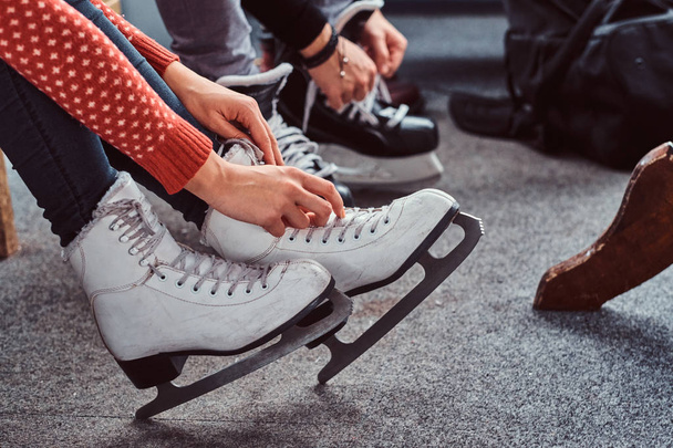 Young couple preparing to a skating. Close-up photo of their hands tying shoelaces of ice hockey skates in the locker room - Φωτογραφία, εικόνα