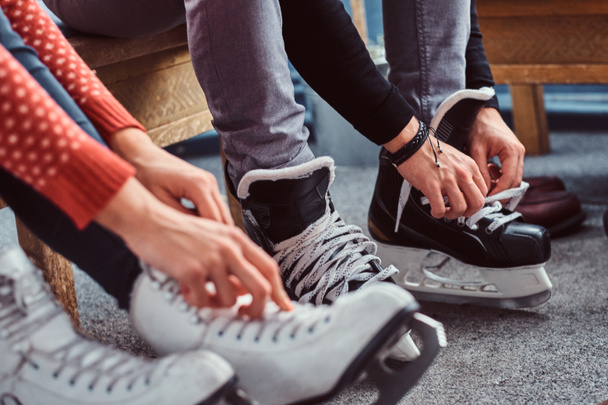 若いカップルがスケートする準備をしています。アイス ホッケーの靴ひもを結ぶ手のクローズ アップ写真は、ロッカー ルームでスケートします。 - 写真・画像