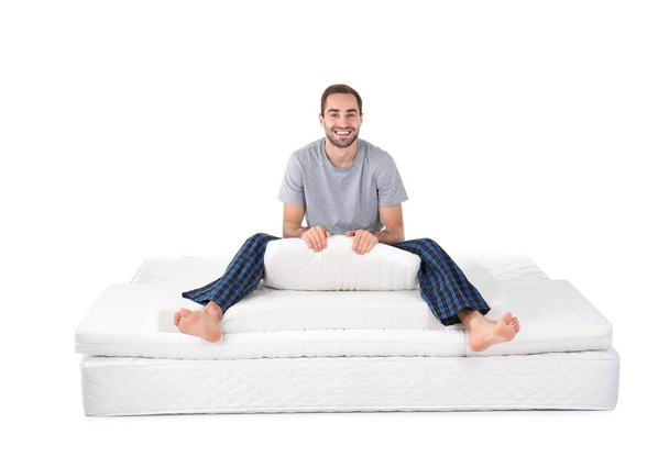 Young man sitting on mattress pile against white background - Φωτογραφία, εικόνα