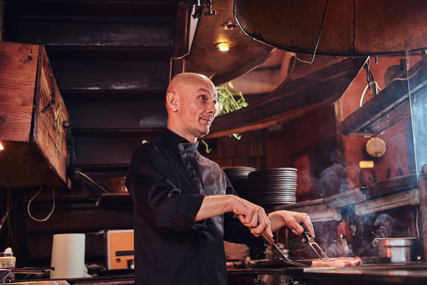 Meesterkok dragen van uniform koken heerlijke biefstuk op een keuken in een restaurant. - Foto, afbeelding