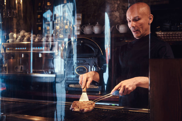 Chef cucinare deliziosa bistecca di manzo su una cucina, in piedi dietro vetro protettivo in un ristorante
. - Foto, immagini