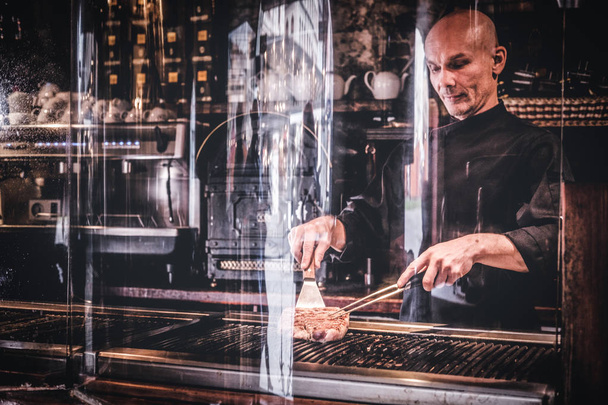 Chef cuisinier délicieux steak de bœuf sur une cuisine, debout derrière un verre de protection dans un restaurant
. - Photo, image
