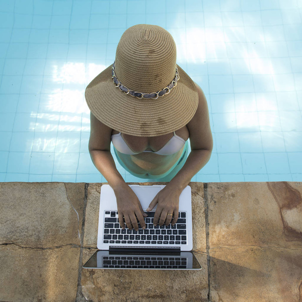 mujer de mediana edad que trabaja en el portátil dentro de la piscina en un día de verano muy caluroso
 - Foto, imagen