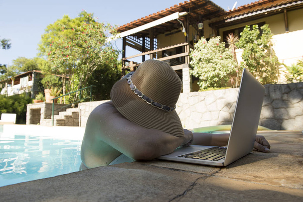 mujer de mediana edad que trabaja en el portátil dentro de la piscina en un día de verano muy caluroso, casi renunciar al trabajo
 - Foto, imagen