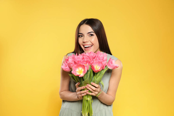 Portrait of beautiful smiling girl with spring tulips on yellow background. International Women's Day - Foto, afbeelding