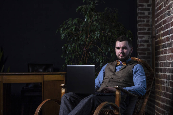 Jeune homme beau avec ordinateur portable assis dans une chaise berçante sur fond de mur de briques
 - Photo, image