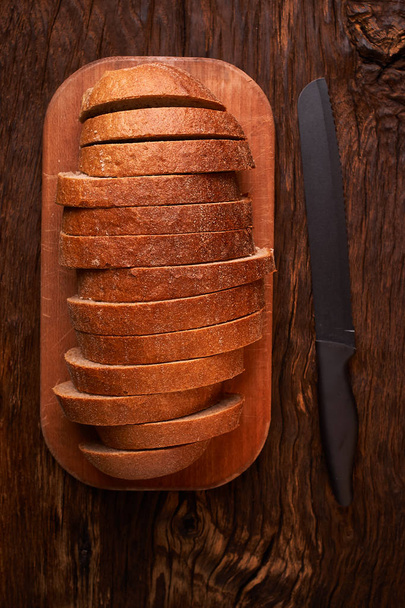 Pan rebanado sobre una mesa de madera y sobre un fondo negro
 - Foto, Imagen