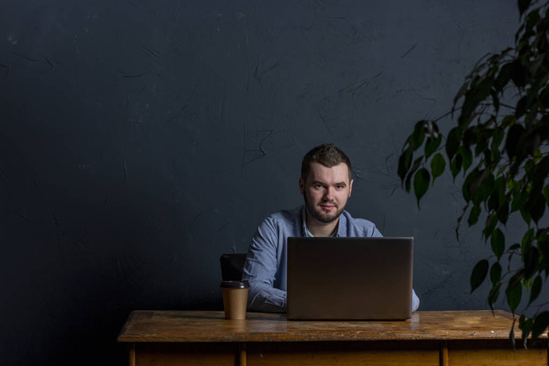 Jeune homme d'affaires travaillant sur son ordinateur portable sur une table en bois. De la place pour le texte. Fond sombre. Espace pour le texte
 - Photo, image