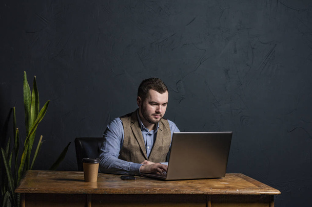 Young businessman working on his laptop on wooden table. Room for text. Dark background. Space for Text - Valokuva, kuva