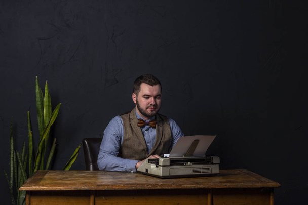 Bearded stylish writer typing on typewriter. Modern writer working on new book in office. Dark background. Space for text - Zdjęcie, obraz